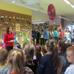 Dzieci zgromadzone przed ścianą wystawową słuchają wypowiedzi pracownika biblioteki