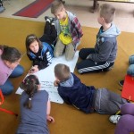 Dzieci piszą na dużym arkuszu papieru ułożonym na podłodze