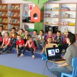 Dzieci siedzą na chidkach i oglądają prezentację na ekranie