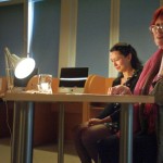 Aktorki grają siedząc przy stole oświetlonym przez lampkę biurkową