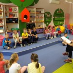 Dzieci podzieleni w grupki słuchają poleceń bibliotekarki