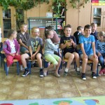 Dzieci siedzą na krzesełkach w sali szkolnej