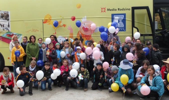 Zdjęcie grupowe dzieci trzymających balony, bibliotekarzy i opiekunów na tle książkobusa