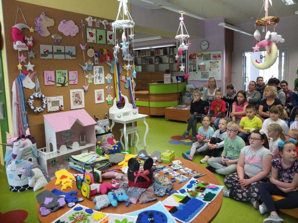 Zdjęcie grupowe dzieci z opiekunami siedzącymi przed wystawą zabawek