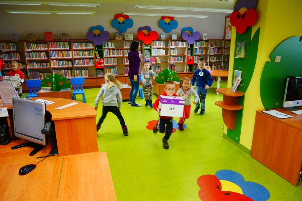 Dzieci biegają po bibliotece, niektóre dzieci trzymają kartony