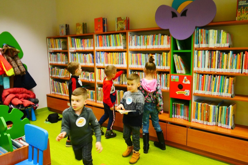 Dzieci wędrują po bibliotece i przeszukują regały z książkami