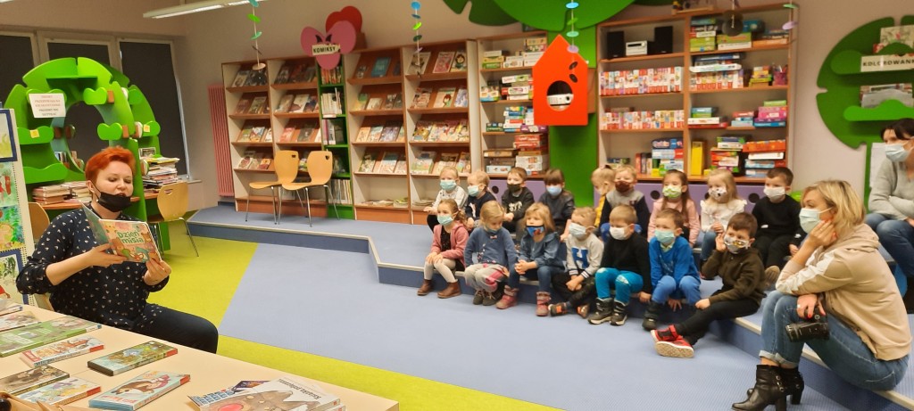 Bibliotekarz pokazuje siedzącym dzieciom obrazki z książki o misiach