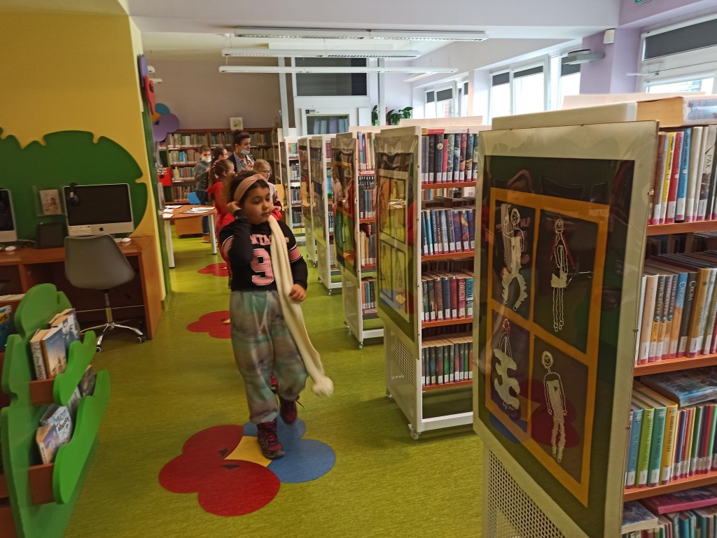 Dzieci oglądają wystawę na planaszach ustawionych na bocznych ściankach regałów z książkami
