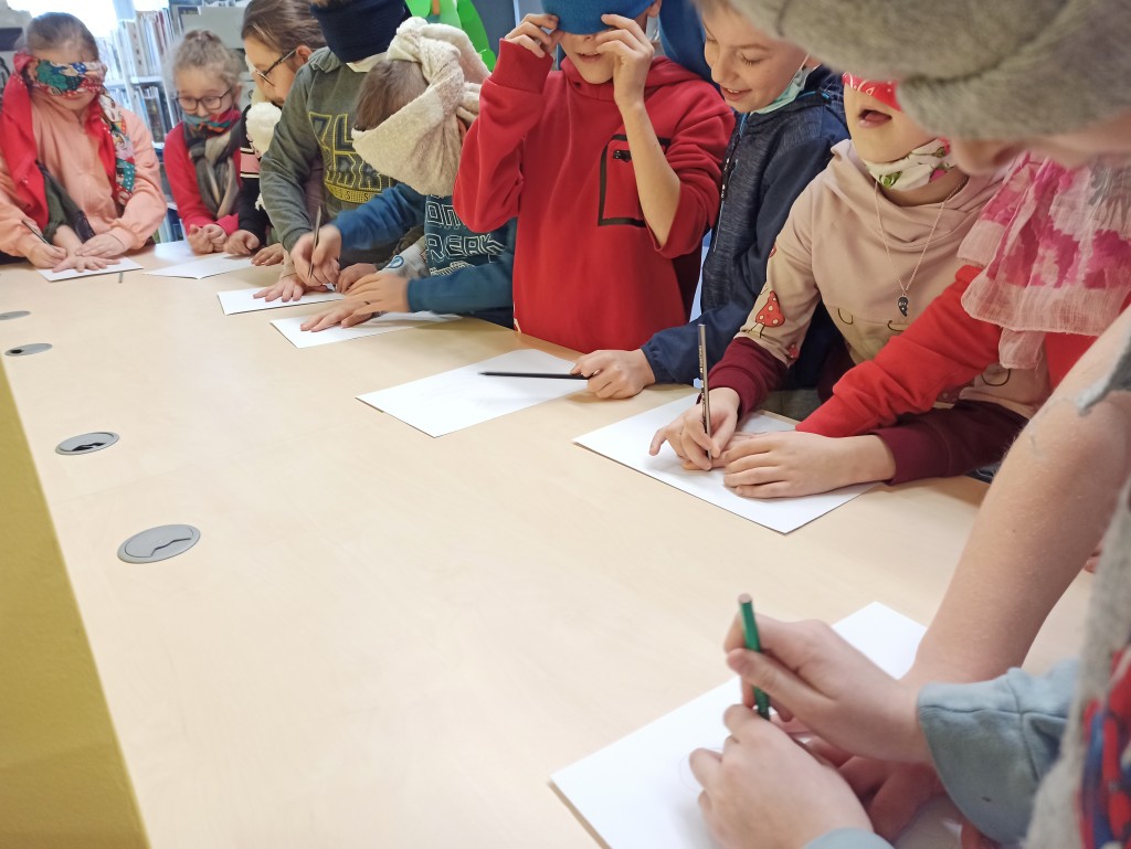 Dzieci przy stole wykonują zadanie polegające na obrysowywaniu na kartce ręki ołówkiem