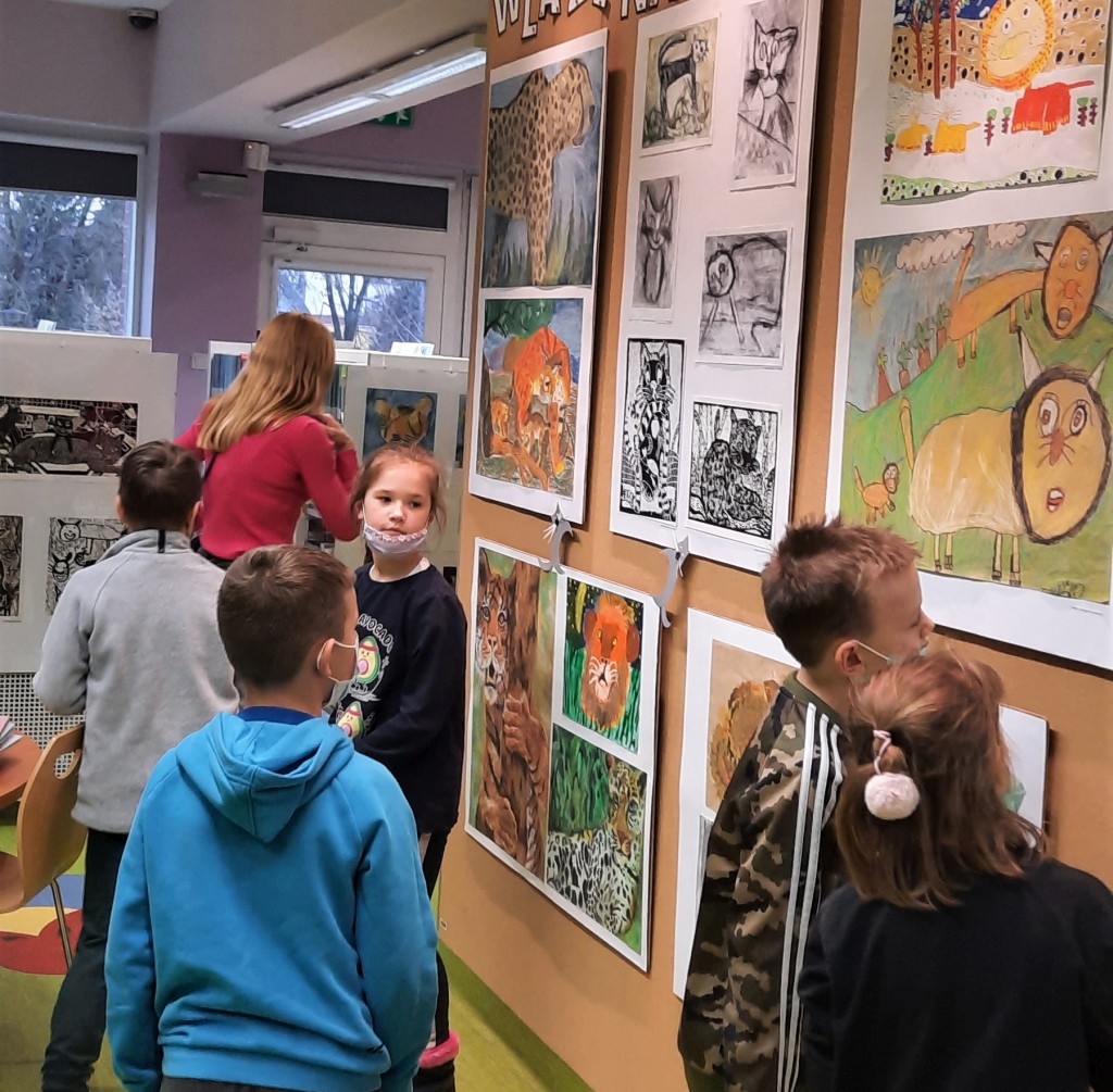 4 dzieci ogląda ścianę wystawową z pracami o kociej tematyce