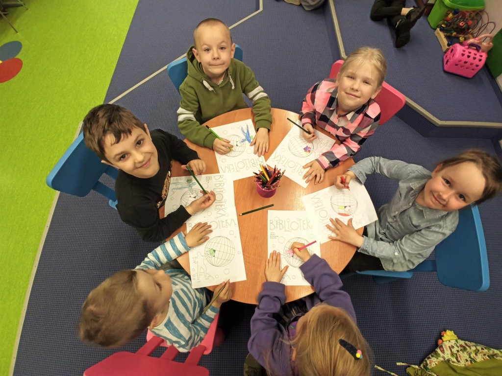 Zdjęcie od góry na okrągły stolik, przy którym siedzi 5 dzieci i rysują plakaty