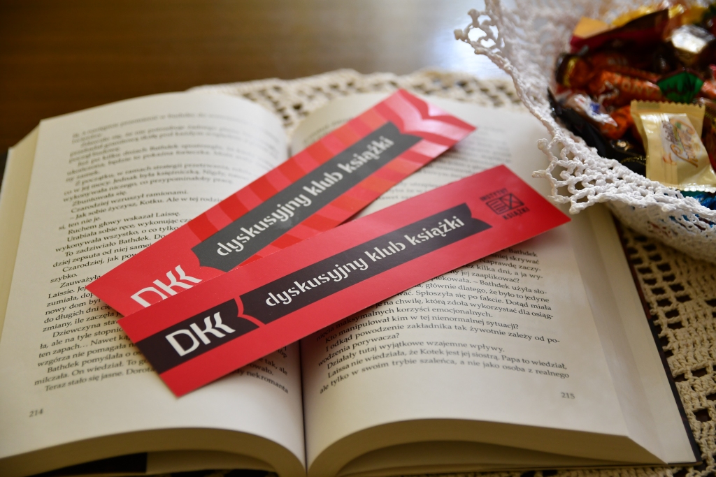 Otwarta książka, na niej położone 2 zakładki DKK, obok w haftowanej misie leżą słodycze