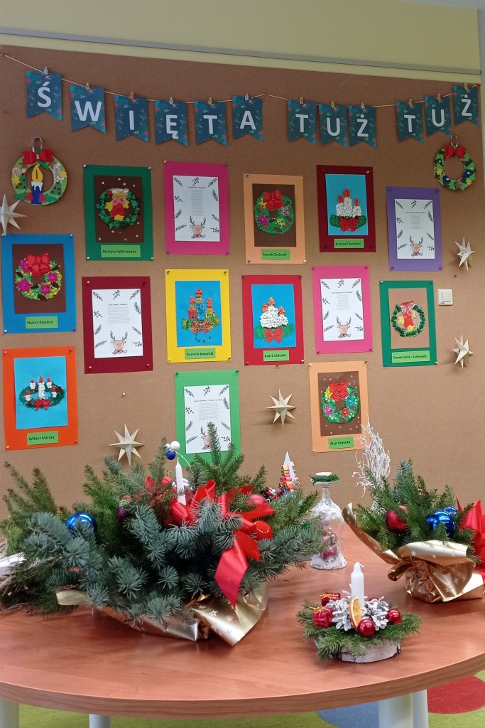 Ściana wystawowa z napisem "Święta tuż tuż" i z rysunkami stroików świątecznych; przed nią okrągły stół z ozdobami świątecznymi
