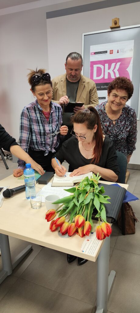 Autorka Ewa Cielesz siedzi przy stoliku i podpisuje książki