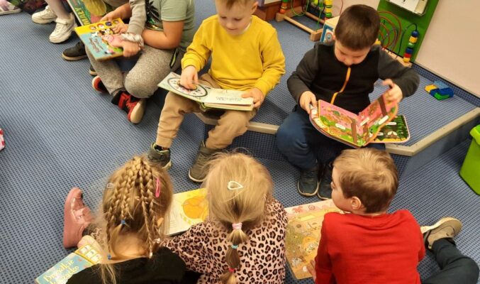 grupa dzieci siedzi na podłodze i czyta książki